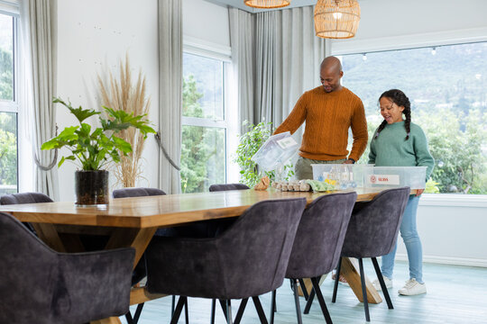 African American father and daughter sorting plastic and glass bins at dining table, copy space