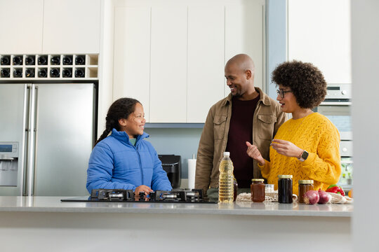 Diverse family standing at kitchen island preparing meal using built-in gas stove, spice jars