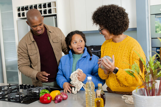 Diverse family standing at kitchen island holding jar lids while arranging peppers in mesh bag