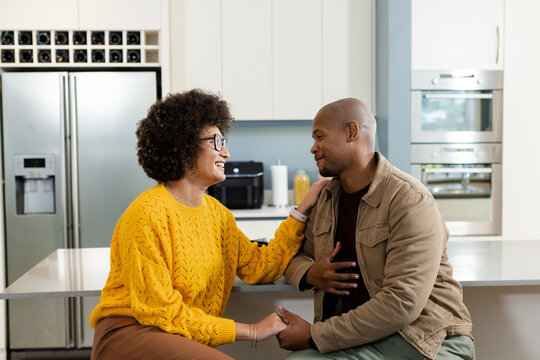 Diverse couple holding hands and chatting at modern kitchen island near fridge and air fryer