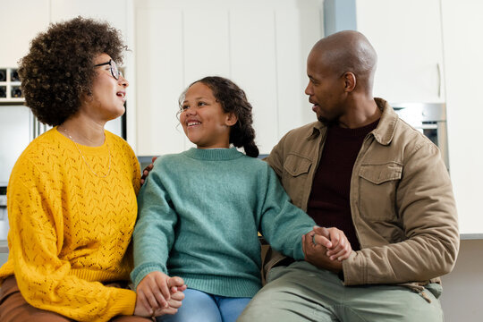 Diverse family wearing knit sweaters holding hands and smiling in kitchen near stainless steel oven