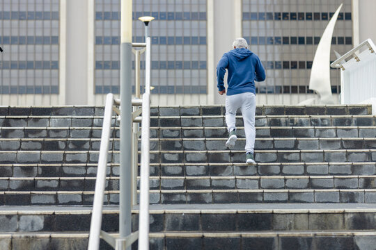 Senior african american mature male running up concrete steps using handrails near office building