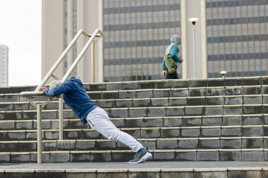 Senior african american man doing inclined push-ups on metal handrail at plaza stairs