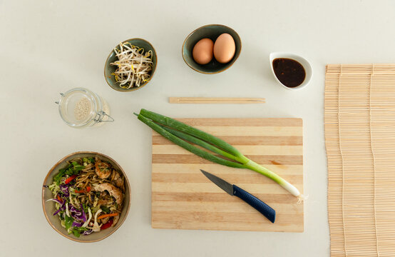 Top-down on kitchen countertop showing cutting board with two scallions and blue-handled knife