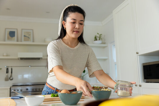 Vertical video: Reaching woman grabbing bowl on counter, holding jar prepping eggs in striped top