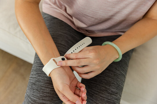 African American woman fastening white smartwatch strap on left wrist on sofa preparing workout