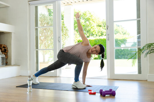 Adult African American woman in sportswear performing twisted lunge on mat at home with weights
