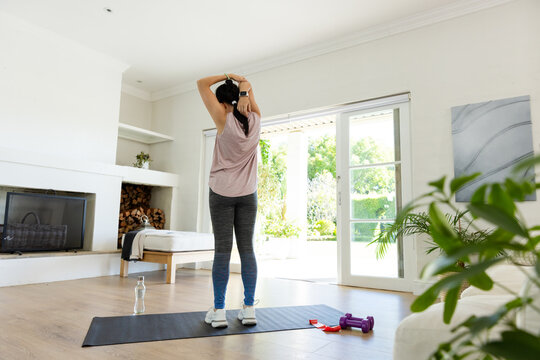 African American woman stretching on black exercise mat in living room wearing pink top