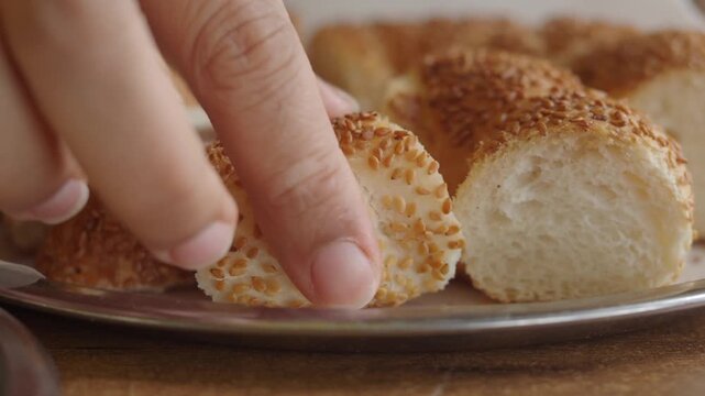 Close up on delicious Turkish bagels with sesame seeds on plate, hand taking a piece