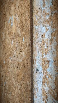 Vertical pan of OSB wood panel texture. Industrial oriented strand board surface with white paint splatters. Construction material close-up.