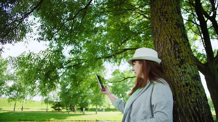 Woman Using Smartphone While Sitting Against Tree in Park, have fun and enjoy © vla