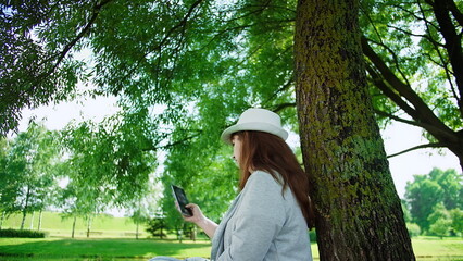 Woman Using Smartphone Outdoors Near Tree in Green Park, have fun and enjoy © vla