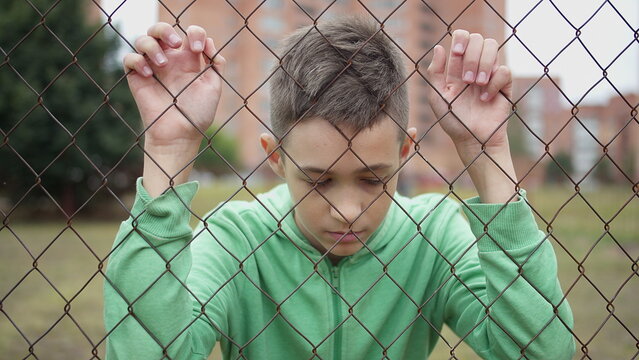 Sad boy standing behind chain link fence, have fun and enjoy