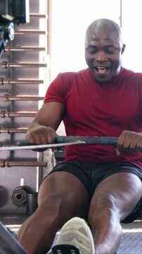 Vertical video: Rowing man in red shirt starting workout, driving legs and pulling on rower at gym
