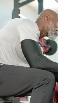 Vertical video: Leaning coach with compression sleeves spotting client starting lift on gym bench