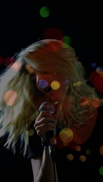 Lead singer gripping wired mic and performing live music on dark stage, colorful bokeh overlaying