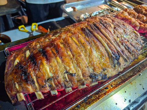 Large pieces of pork ribs are grilling on a grate over hot, glowing coals.