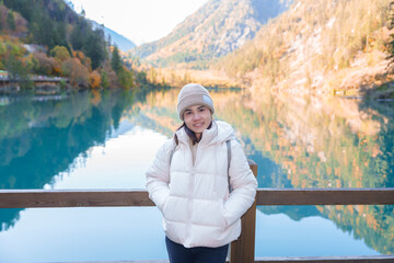 Naklejka premium Happy woman traveler travel in jiuzhaigou national park in Sichuan, China. Tourist sightseeing Panda lake and snow mountain in Autumn season. Famous Landmark and Vacation near Chengdu, China