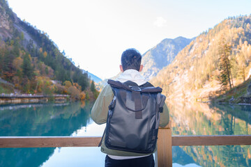 Naklejka premium Happy man traveler travel in jiuzhaigou national park in Sichuan, China. Tourist sightseeing Panda lake and snow mountain in Autumn season. Famous Landmark and Vacation near Chengdu, China