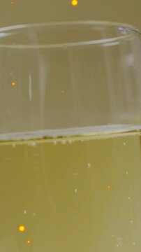 Vertical video: Camera revealing glass while bubbles rising and amber sparks drifting for drink ad