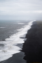 Fototapeta premium Black sand and oceanic water on Reynisfjara beach, Iceland views from the Dyrholaey, vertical travel and tourism banner
