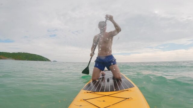 Caucasian young man rows on a paddleboard as glides over the ocean waves.