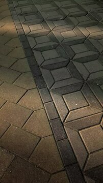 Vertical pan of interlocking paving stones with long diagonal shadows. Urban sidewalk texture in bright sunlight.