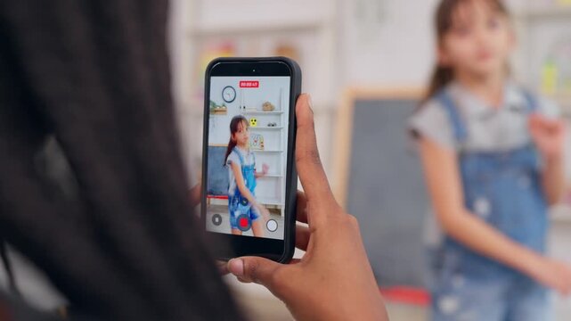 African teacher use phone record young child dancing in learning space.