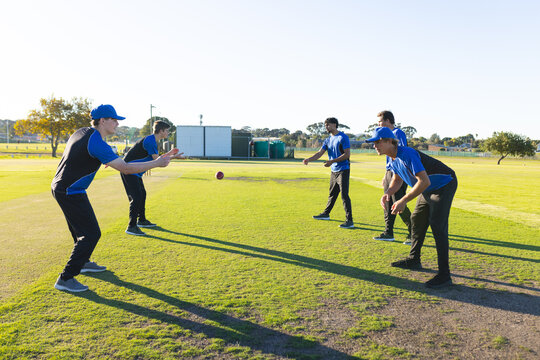 Red training ball soaring across green grass field past portable practice nets, equipment shed
