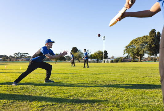 Cricket bat swinging toward midair ball and gloves, on sports field with cones