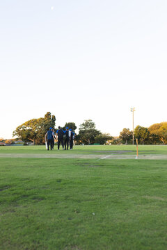Six cricket players in blue jerseys walking across green pitch during afternoon near stumps
