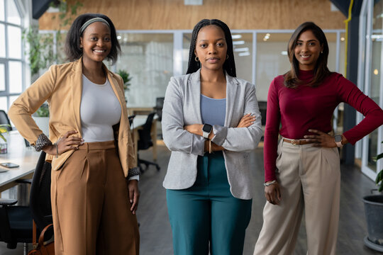 Diverse female coworkers posing in modern open-plan office with computer monitors and smartwatch