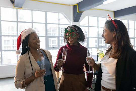 Diverse female staff wearing festive headwear celebrating with champagne flutes in office