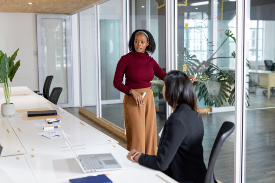 Diverse female colleagues collaborating around office glass partition showing flowcharts and laptop