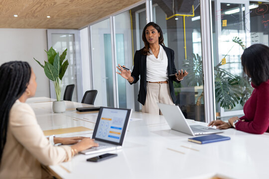Diverse women team presenting sales figures on whiteboard in meeting room with marker, copy space