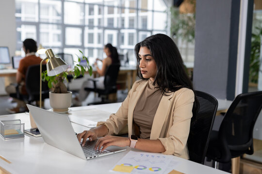 Diverse coworkers working in modern office typing on laptop while using smartphone to review charts