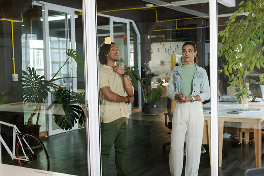 Diverse coworkers analyzing diagrams on board with sticky notes and markers at office near bicycle