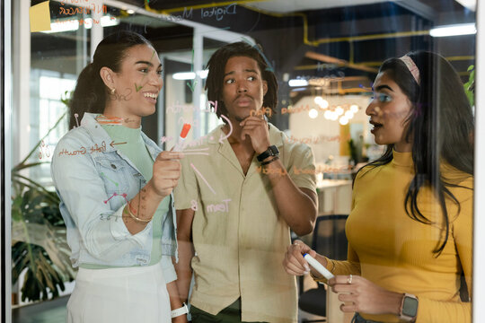 Diverse coworkers in casual attire marking flowchart and discussing ideas on whiteboard in office