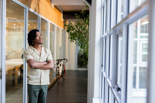 African American man standing with arms crossed in office hallway near bicycle and potted plant