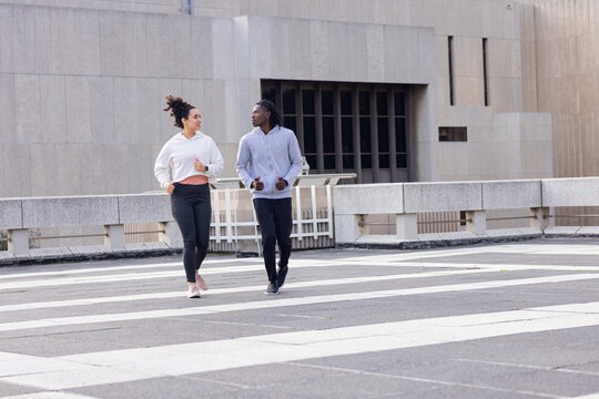 Diverse friends jogging and keeping pace in sportswear on rooftop terrace marked with white stripes