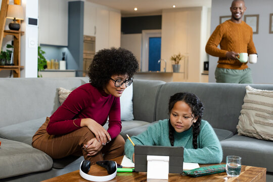 African American family helping daughter with homework at living room coffee table using tablet