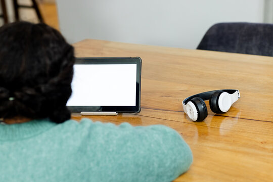 Blank-screen tablet is resting on wooden table, with stylus and headphones occupying office desk