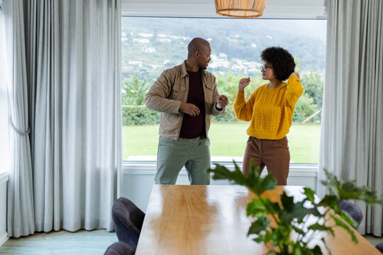 African American couple dancing together at home dining area beside wooden table and potted plant