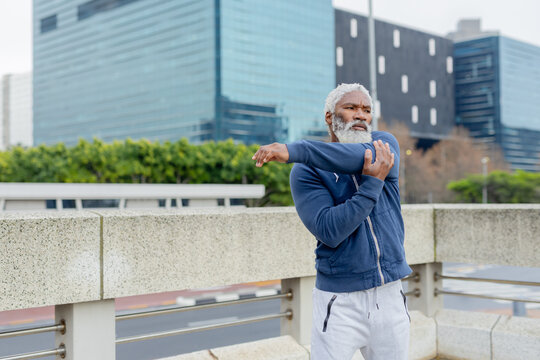 Senior african american man stretching on bridge by railing wearing athletic clothing