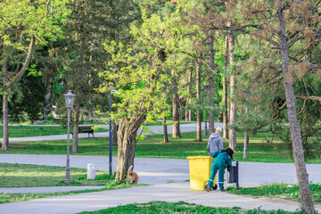 Fototapeta premium Man in a green jacket empties trash into a yellow trash can