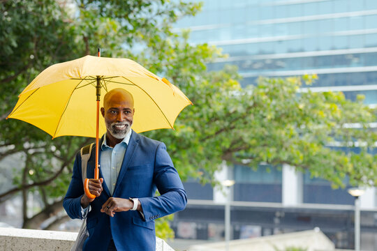 African american man on sidewalk ledge holding yellow umbrella checking watch with bag