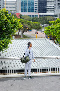 Standing on metal overpass african american man holding duffel bag, talking on phone