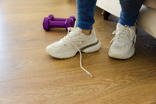 African-American woman at home seeing loose lace tying in leggings for workout near purple dumbbell