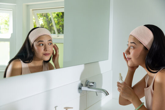 African American woman seeing self in mirror and applying serum with dropper for skincare at vanity