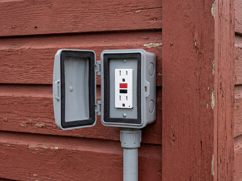 Outdoor GFCI electrical outlet with weatherproof cover on red wood siding